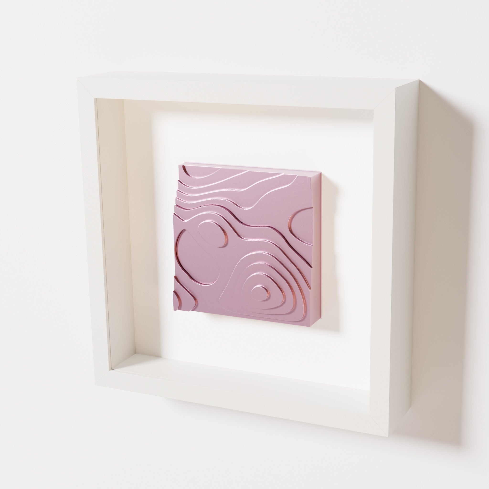 A close-up of a white shadowbox frame containing a metallic rose artwork depicting layered contour lines inspired by geographic elevation levels, showcasing reflective pink details.