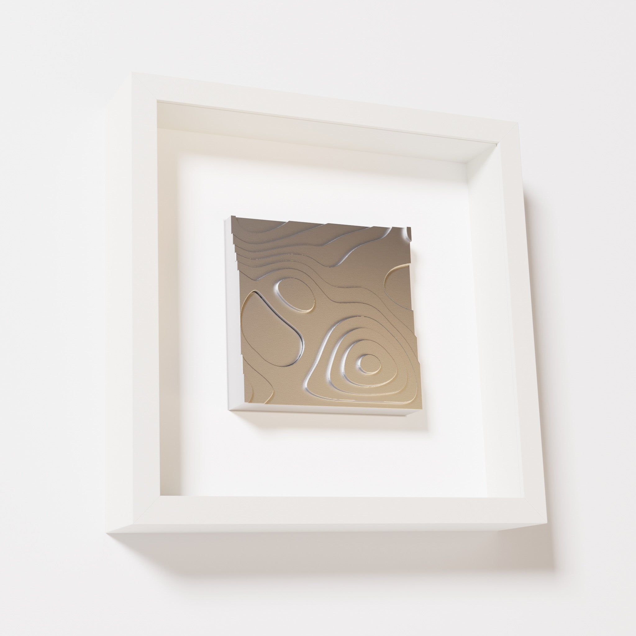 A close-up of a white shadowbox frame containing a chrome silver artwork depicting layered contour lines inspired by geographic elevation levels, showcasing reflective silver details.