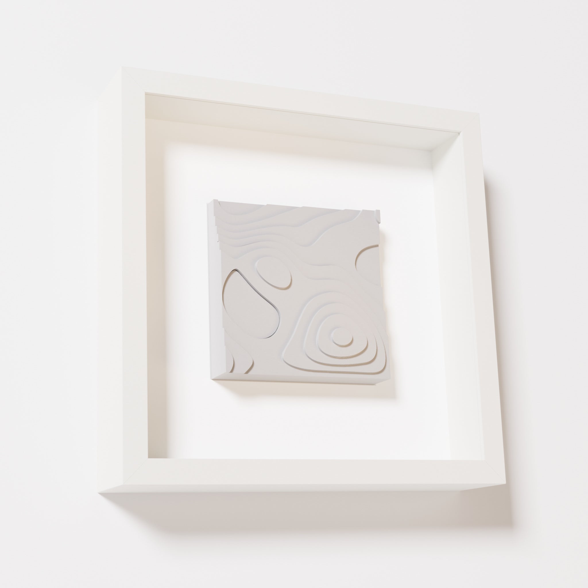 A close-up of a white shadowbox frame containing a marble white artwork depicting layered contour lines inspired by geographic elevation levels, showcasing intricate and geometric details.