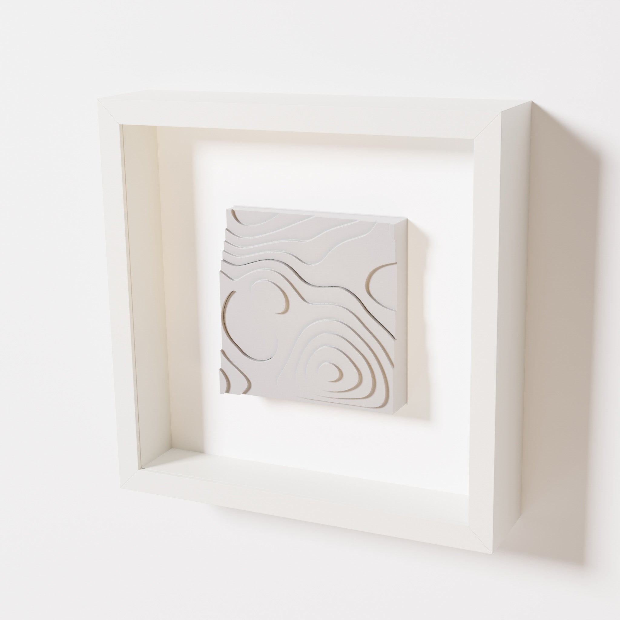 A close-up of a white shadowbox frame containing a marble white artwork depicting layered contour lines inspired by geographic elevation levels, showcasing intricate and geometric details.