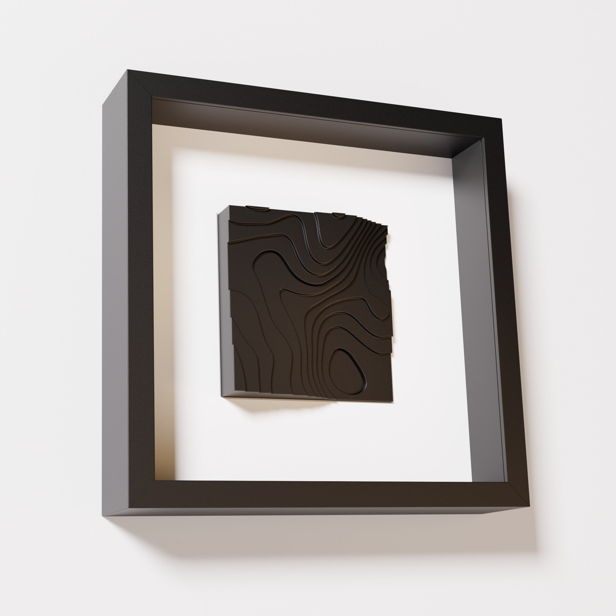 A close-up of a black shadowbox frame containing a matte black artwork depicting flowing contour lines inspired by geographic elevation levels, showcasing intricate geometric details.