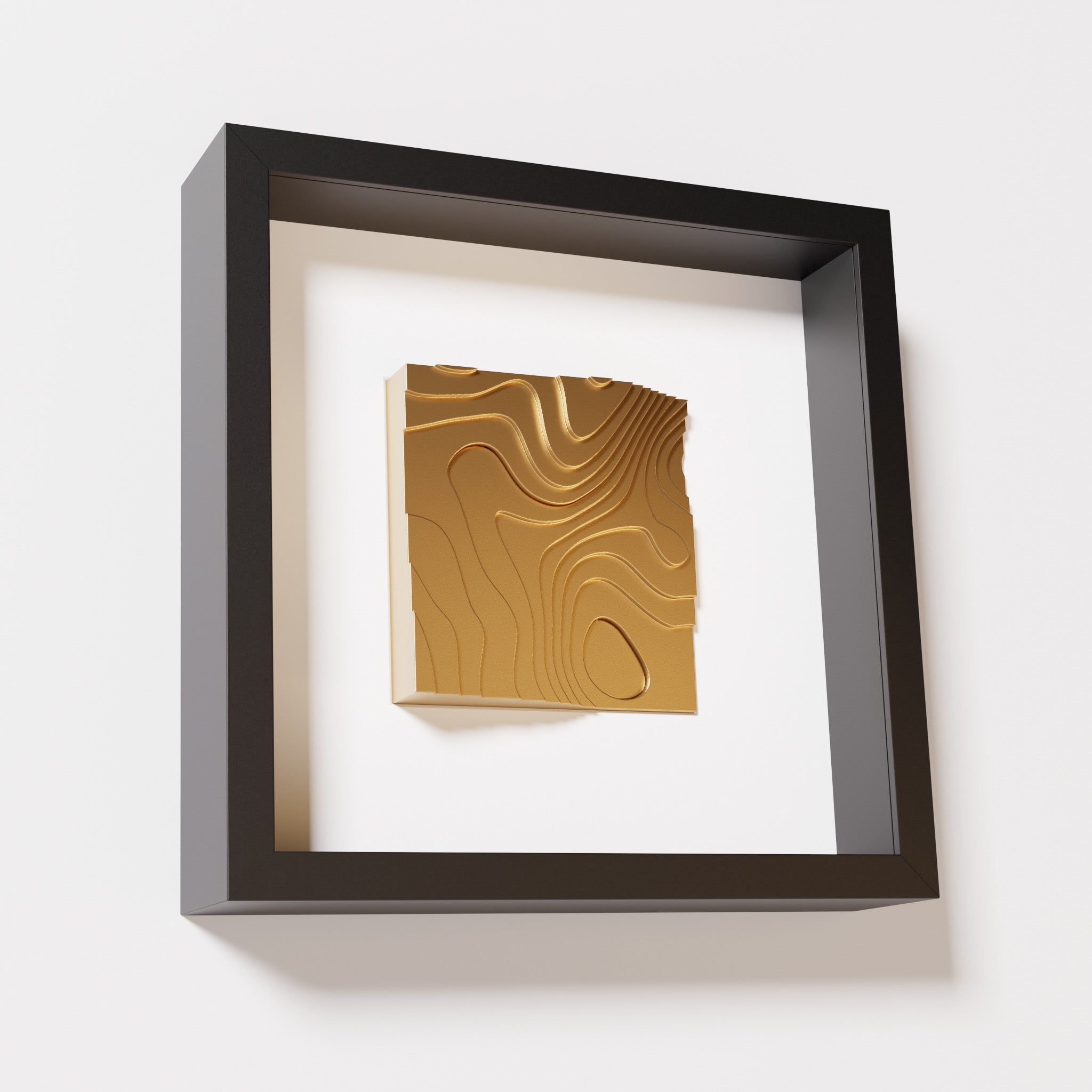 A close-up of a black shadowbox frame containing a chrome gold artwork depicting flowing contour lines inspired by geographic elevation levels, showcasing reflective golden details.