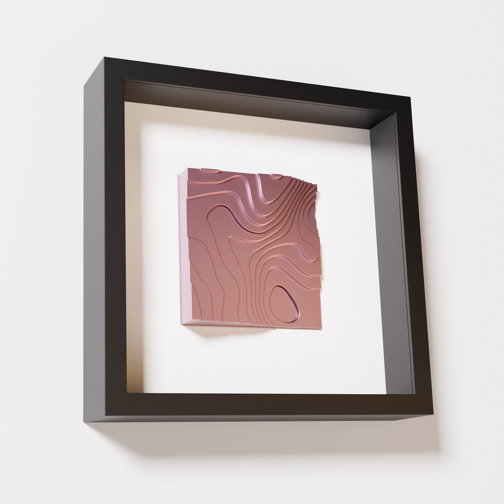 A close-up of a black shadowbox frame containing a metallic rose artwork depicting flowing contour lines inspired by geographic elevation levels, showcasing reflective pink details.