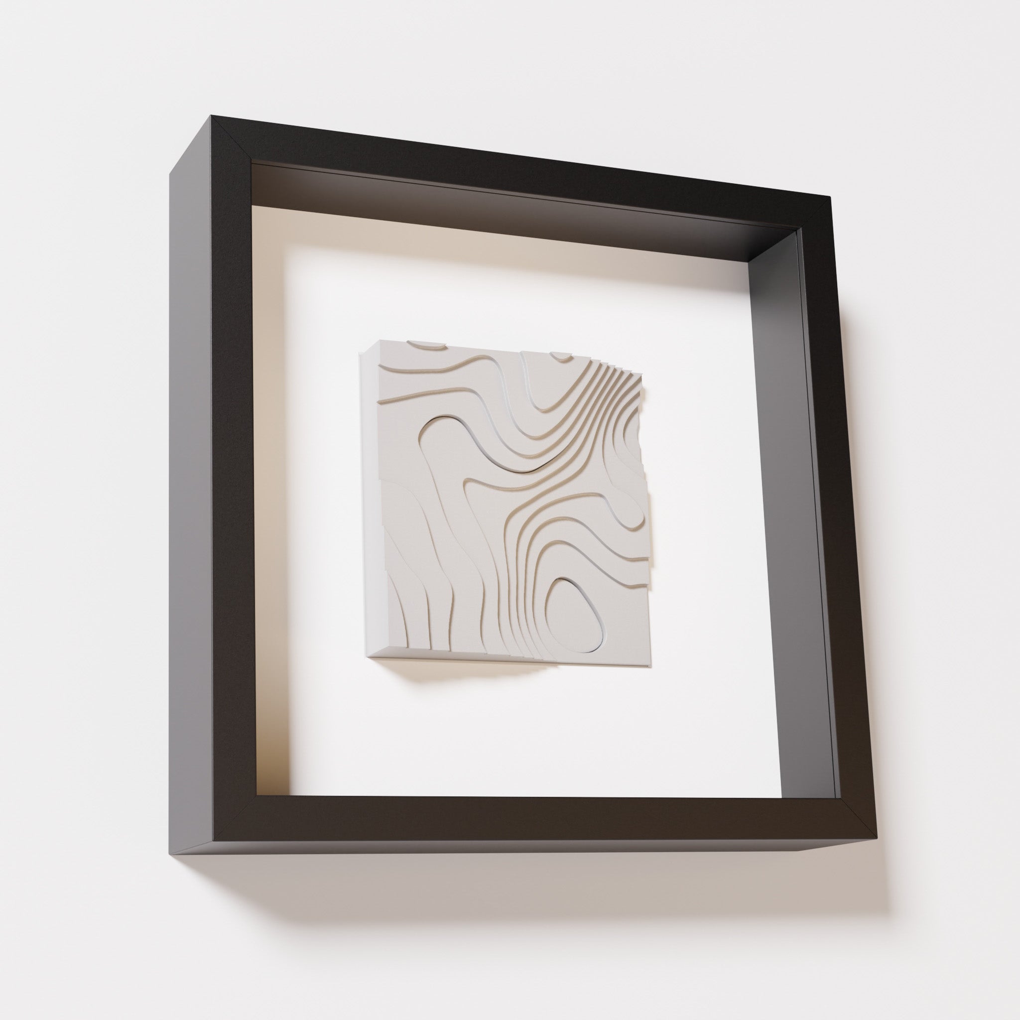 A close-up of a black shadowbox frame containing a marble white artwork depicting flowing contour lines inspired by geographic elevation levels, showcasing intricate geometric details.