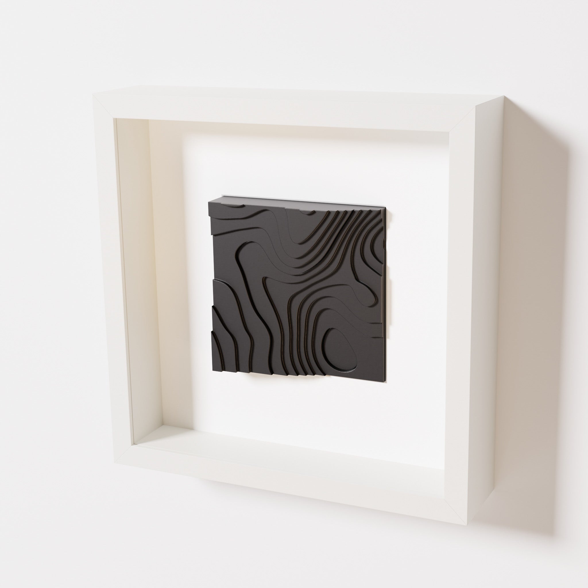 A close-up of a white shadowbox frame containing a matte black artwork depicting flowing contour lines inspired by geographic elevation levels, showcasing intricate geometric details.