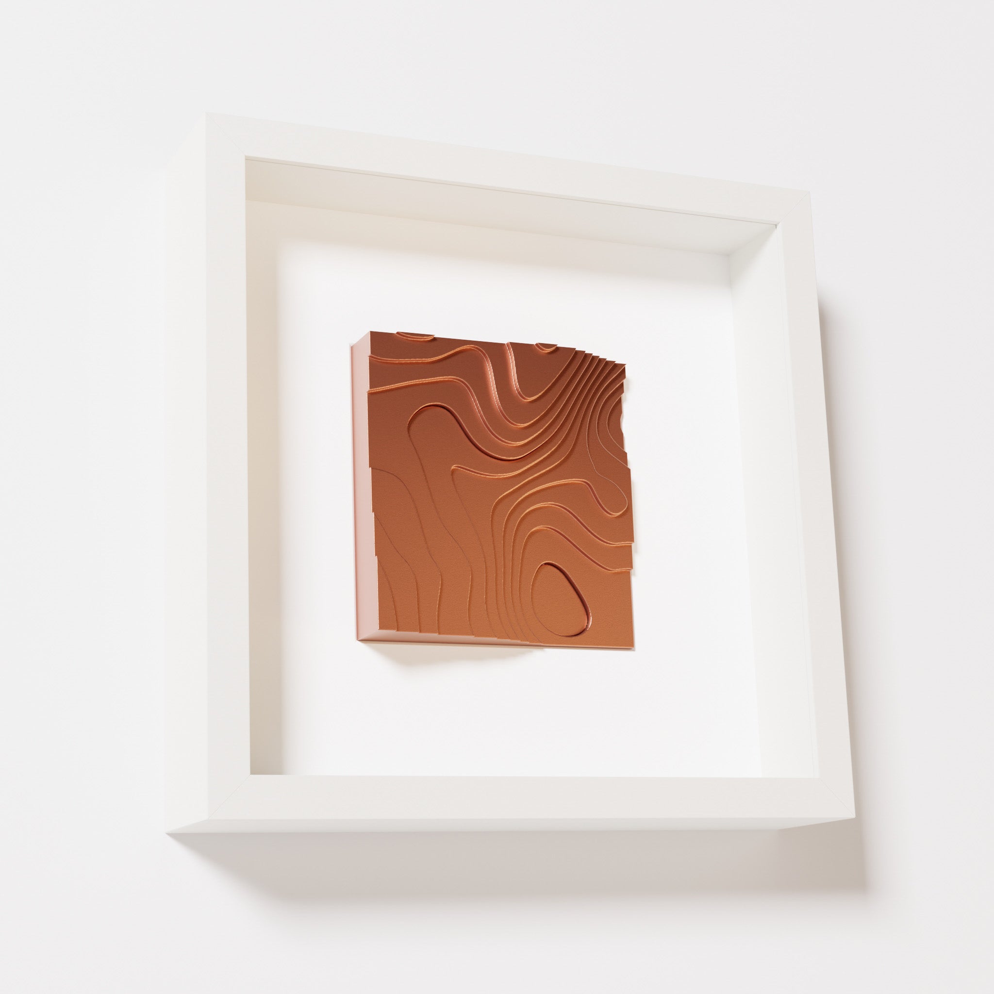 A close-up of a white shadowbox frame containing a chrome copper artwork depicting flowing contour lines inspired by geographic elevation levels, showcasing reflective copper details.