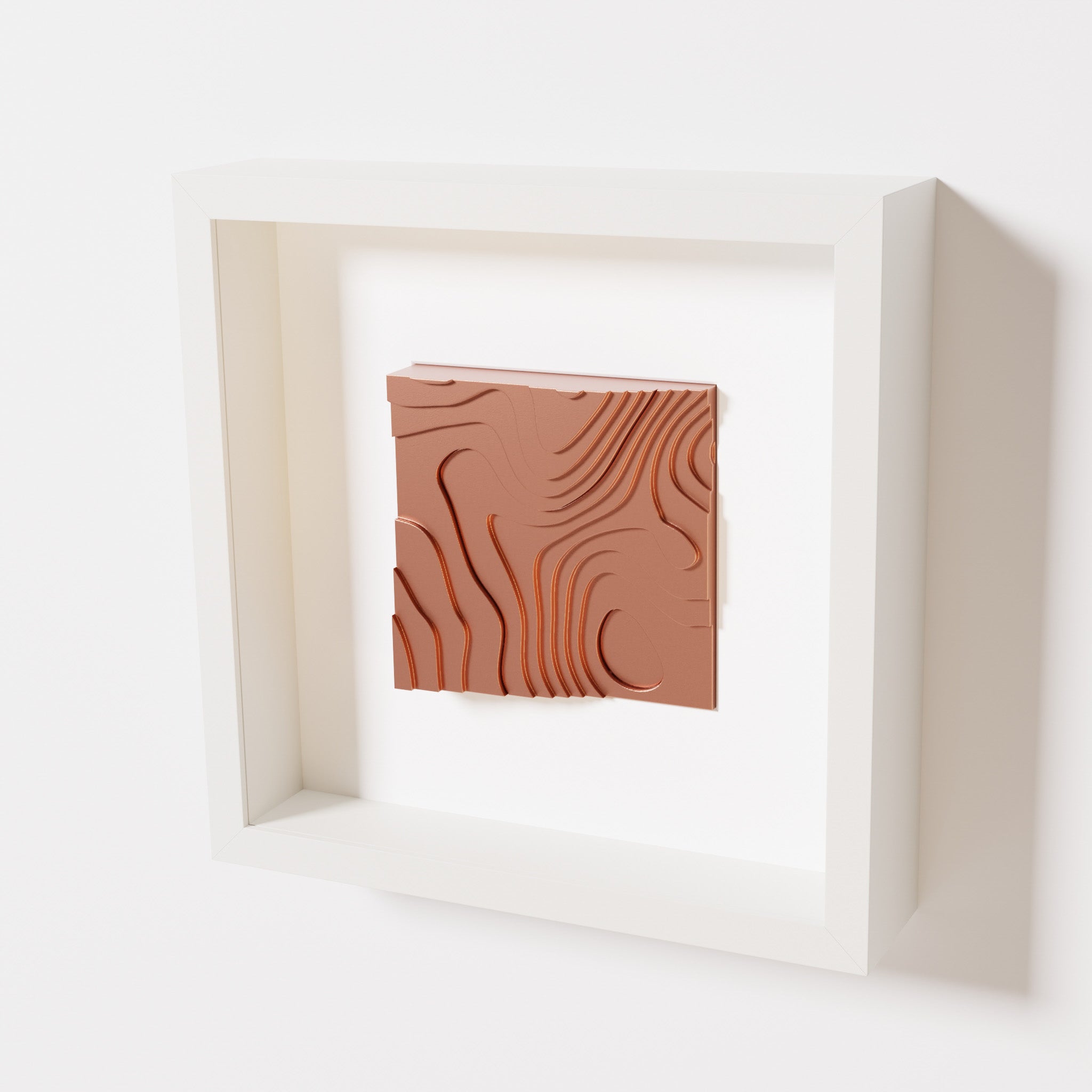 A close-up of a white shadowbox frame containing a chrome copper artwork depicting flowing contour lines inspired by geographic elevation levels, showcasing reflective copper details.