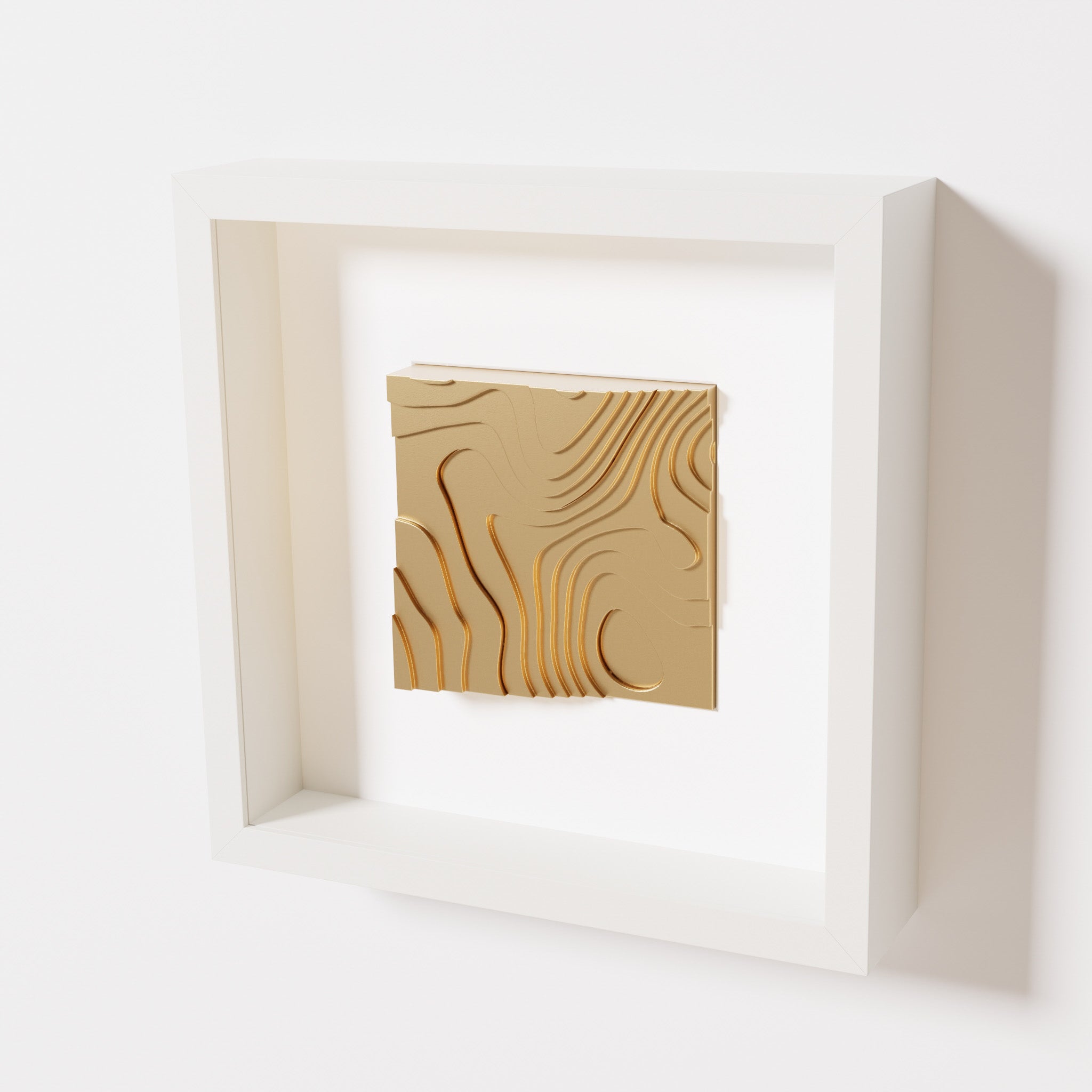 A close-up of a white shadowbox frame containing a chrome gold artwork depicting flowing contour lines inspired by geographic elevation levels, showcasing reflective golden details.