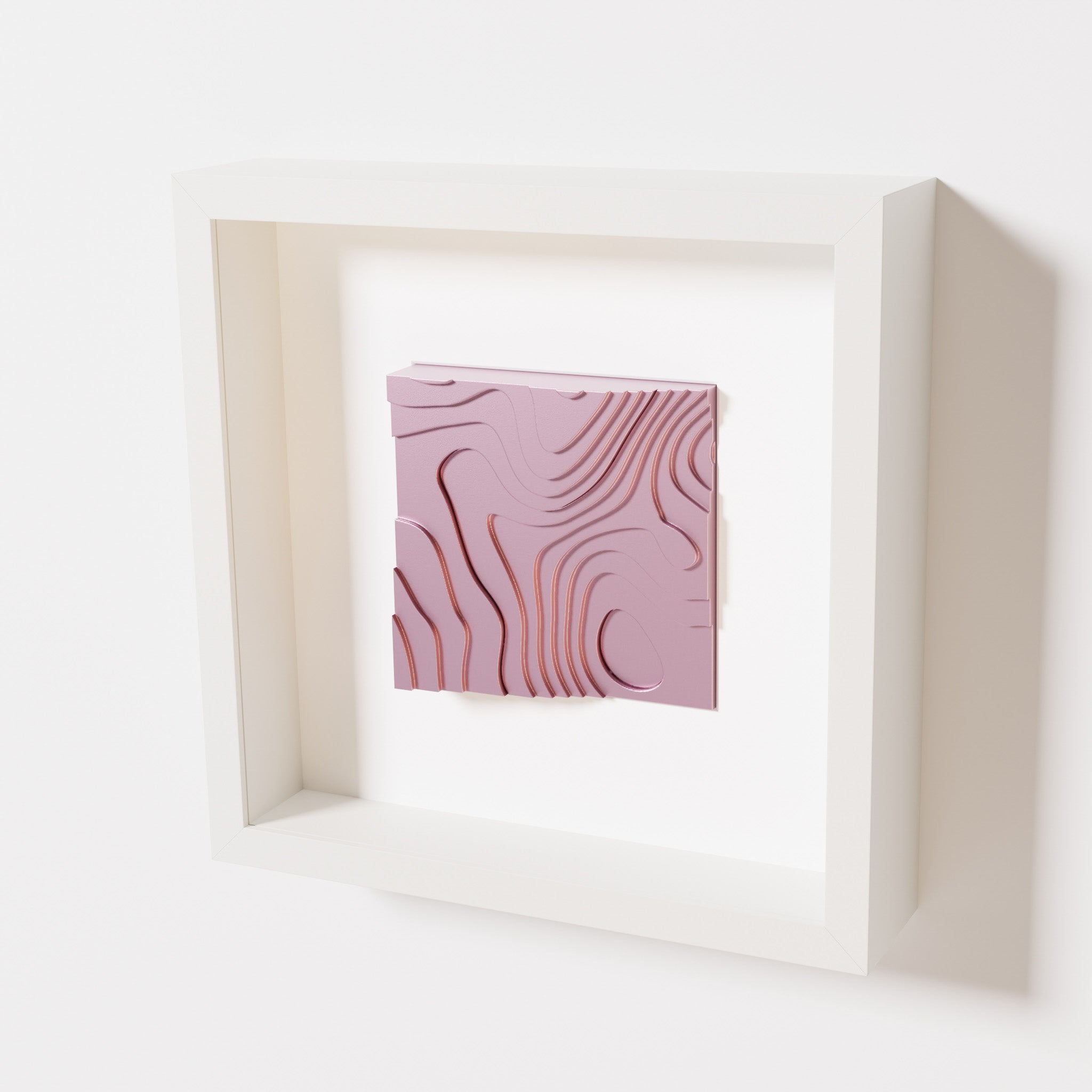 A close-up of a white shadowbox frame containing a metallic rose artwork depicting flowing contour lines inspired by geographic elevation levels, showcasing reflective pink details.