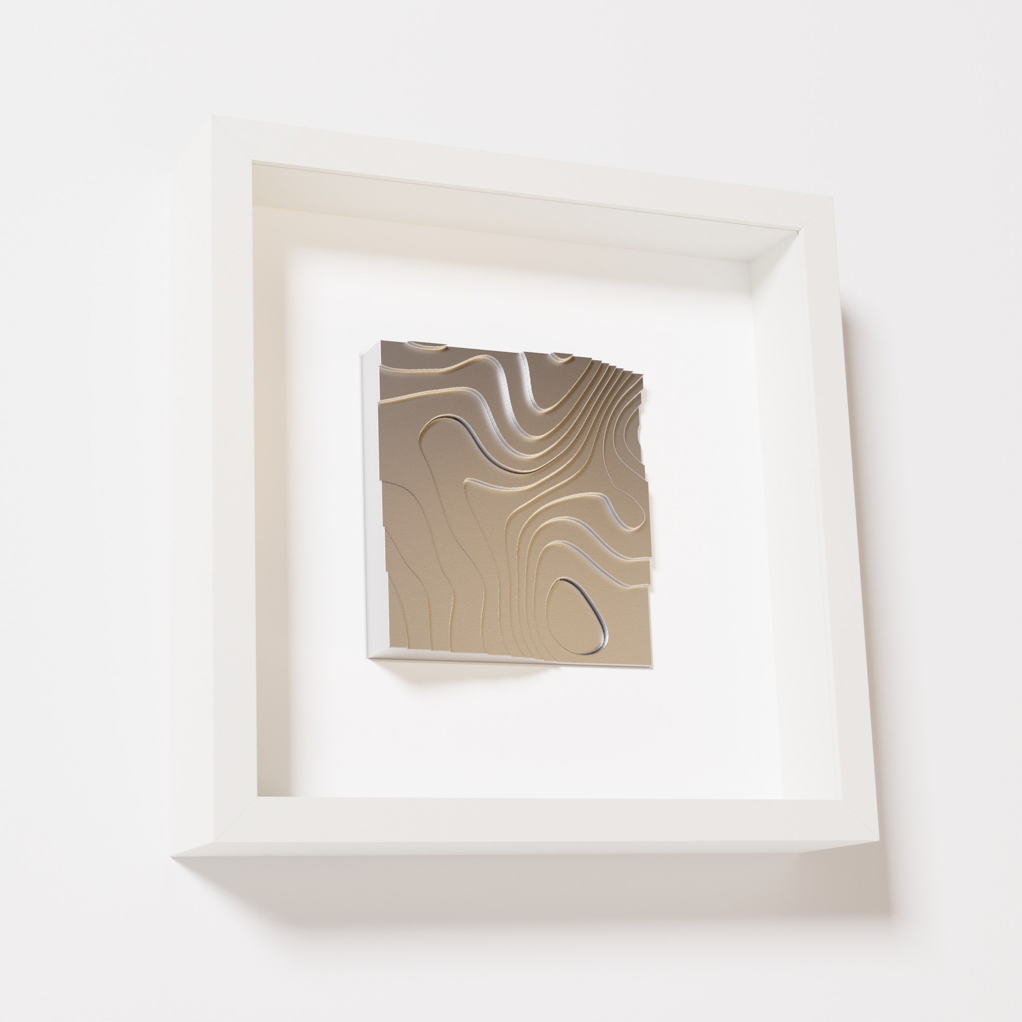 A close-up of a white shadowbox frame containing a chrome silver artwork depicting flowing contour lines inspired by geographic elevation levels, showcasing reflective silver details.