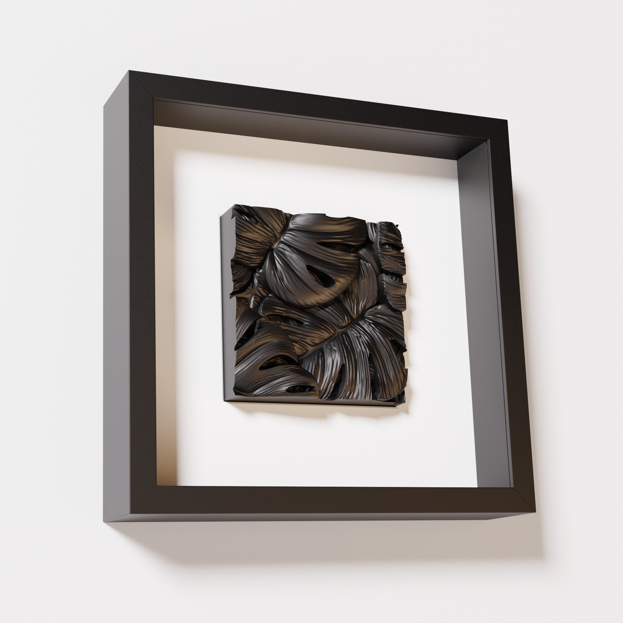 A close-up of a black shadowbox frame containing a matte black artwork featuring layered Monstera leaves, showcasing intricate overlapping details and deep shadows.