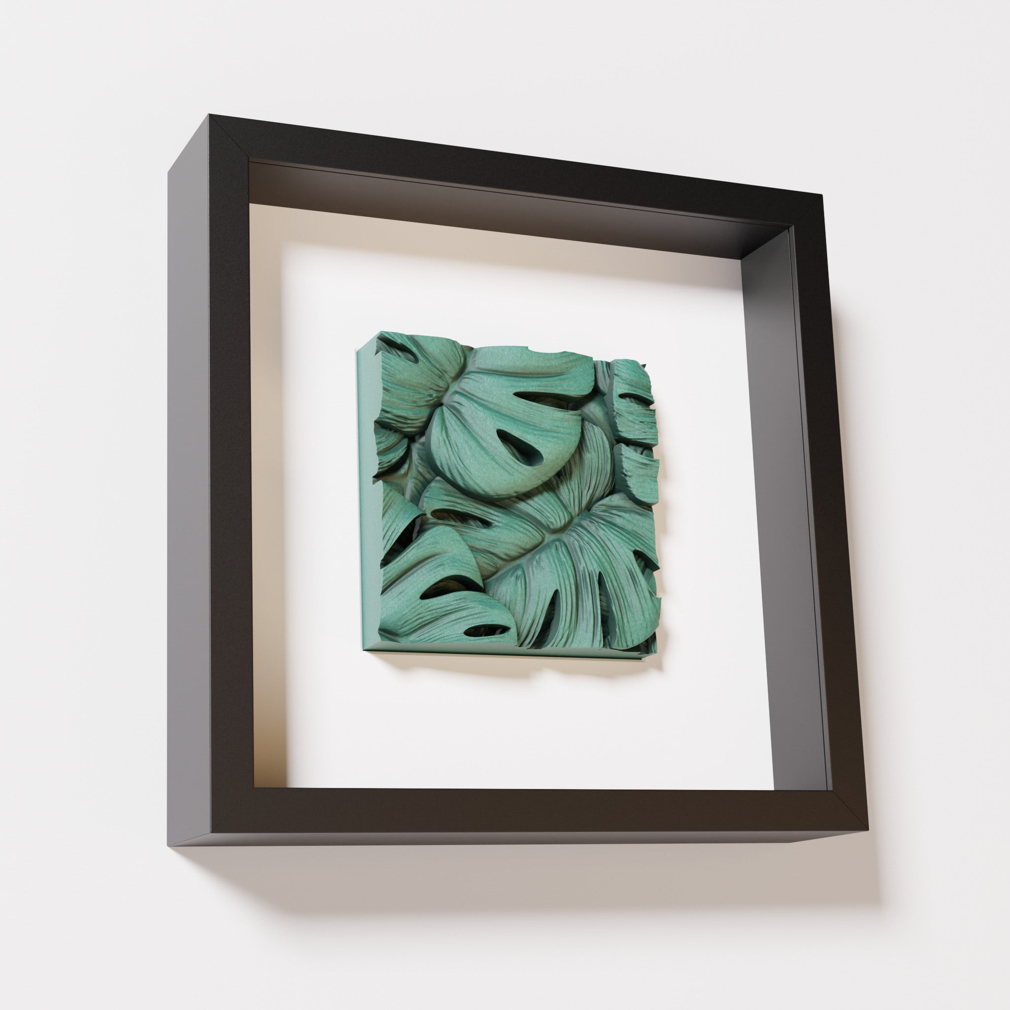 A close-up of a black shadowbox frame containing an old patina artwork featuring layered Monstera leaves, showcasing intricate overlapping details with a textured green finish.