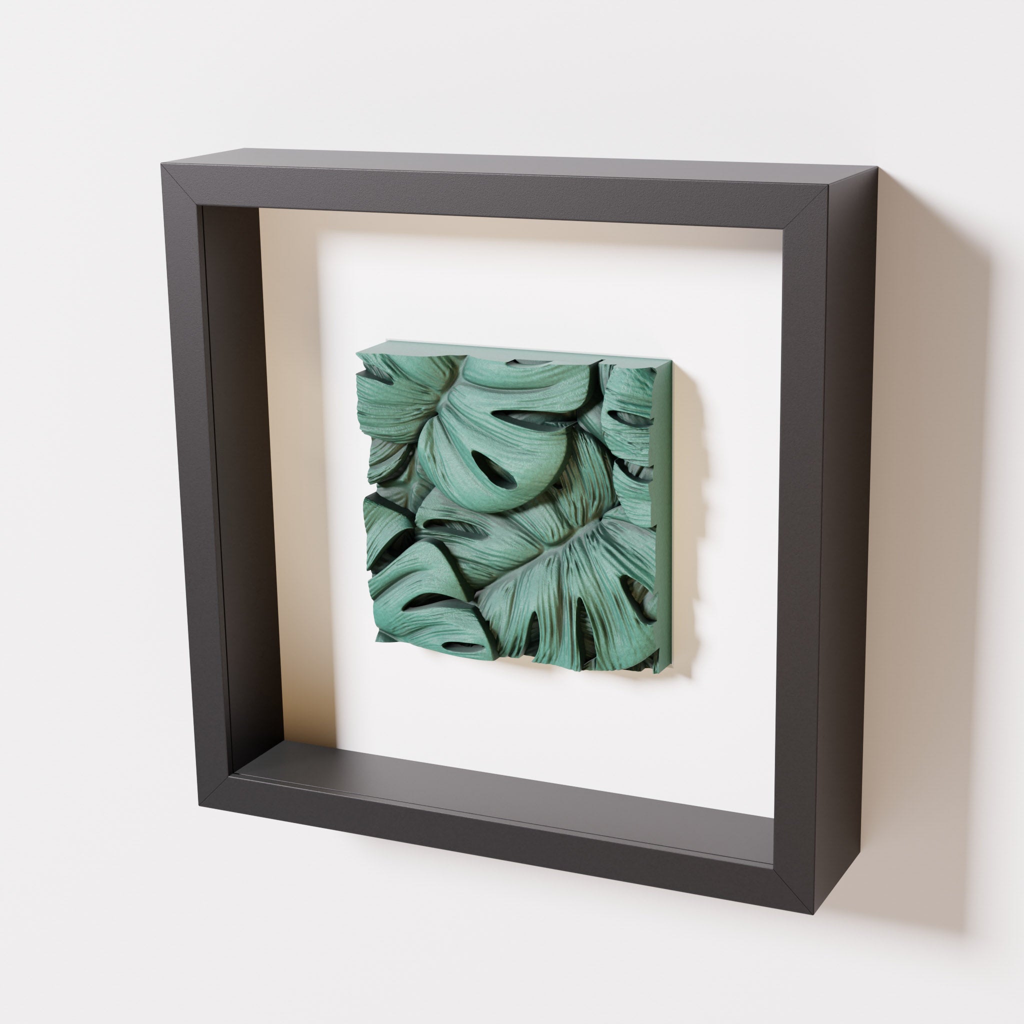 A close-up of a black shadowbox frame containing an old patina artwork featuring layered Monstera leaves, showcasing intricate overlapping details with a textured green finish.