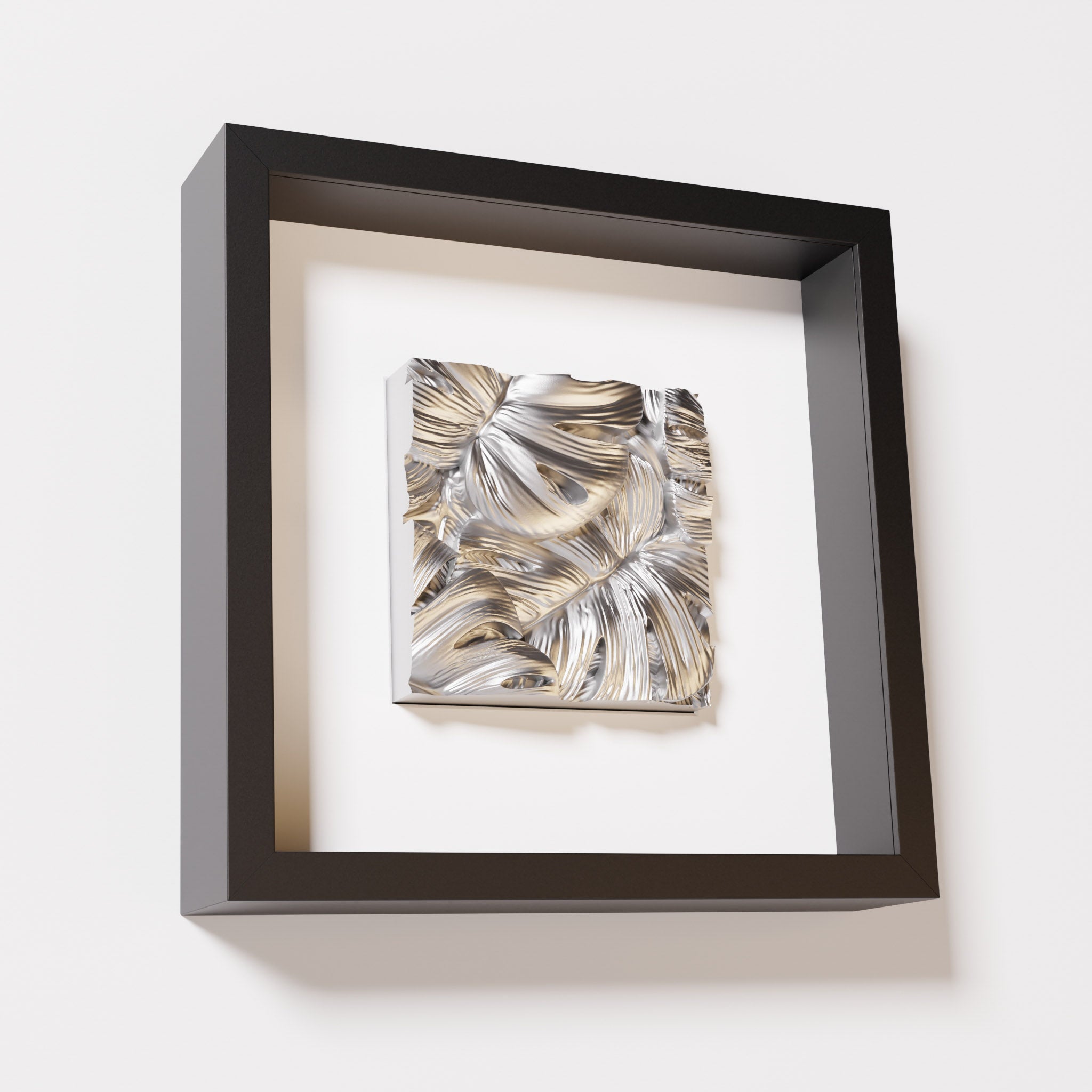 A close-up of a black shadowbox frame containing a chrome silver artwork featuring layered Monstera leaves, showcasing reflective silver highlights and intricate overlapping details.