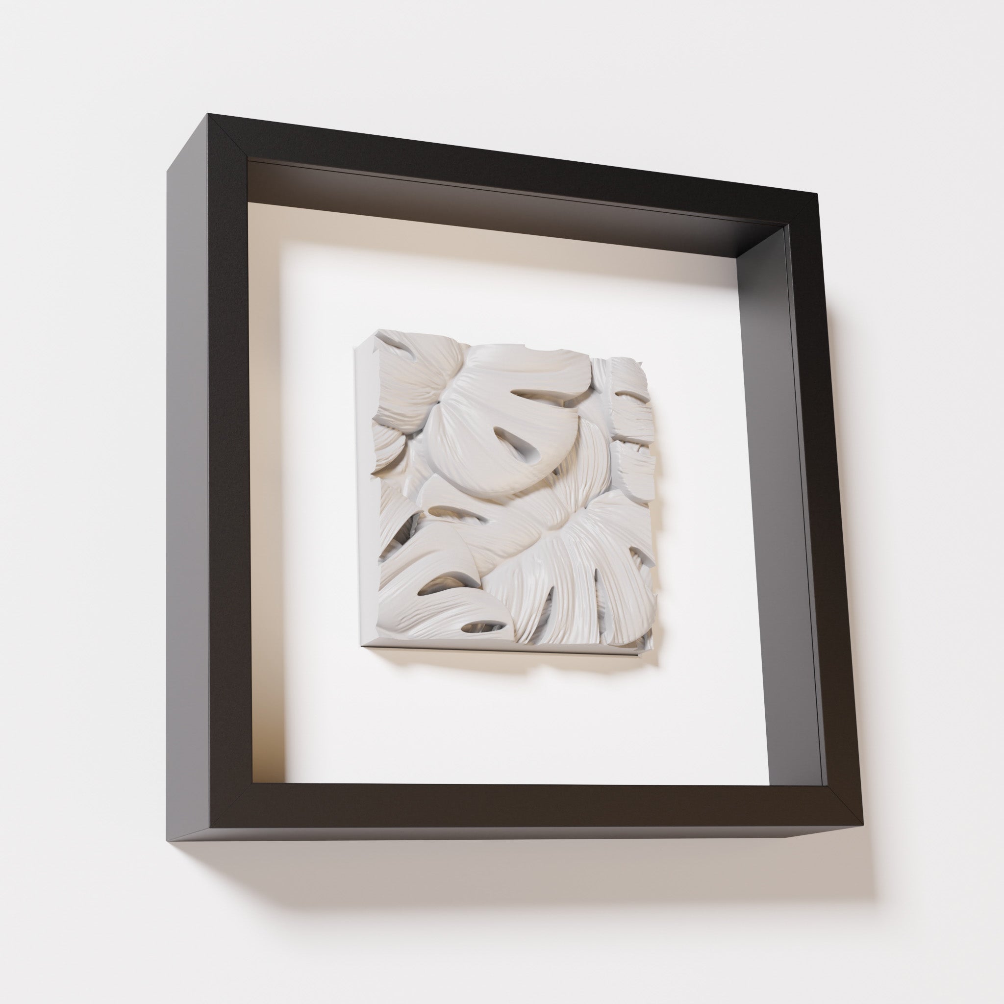 A close-up of a black shadowbox frame containing a marble white artwork featuring layered Monstera leaves, showcasing delicate overlapping details with a soft, smooth texture.