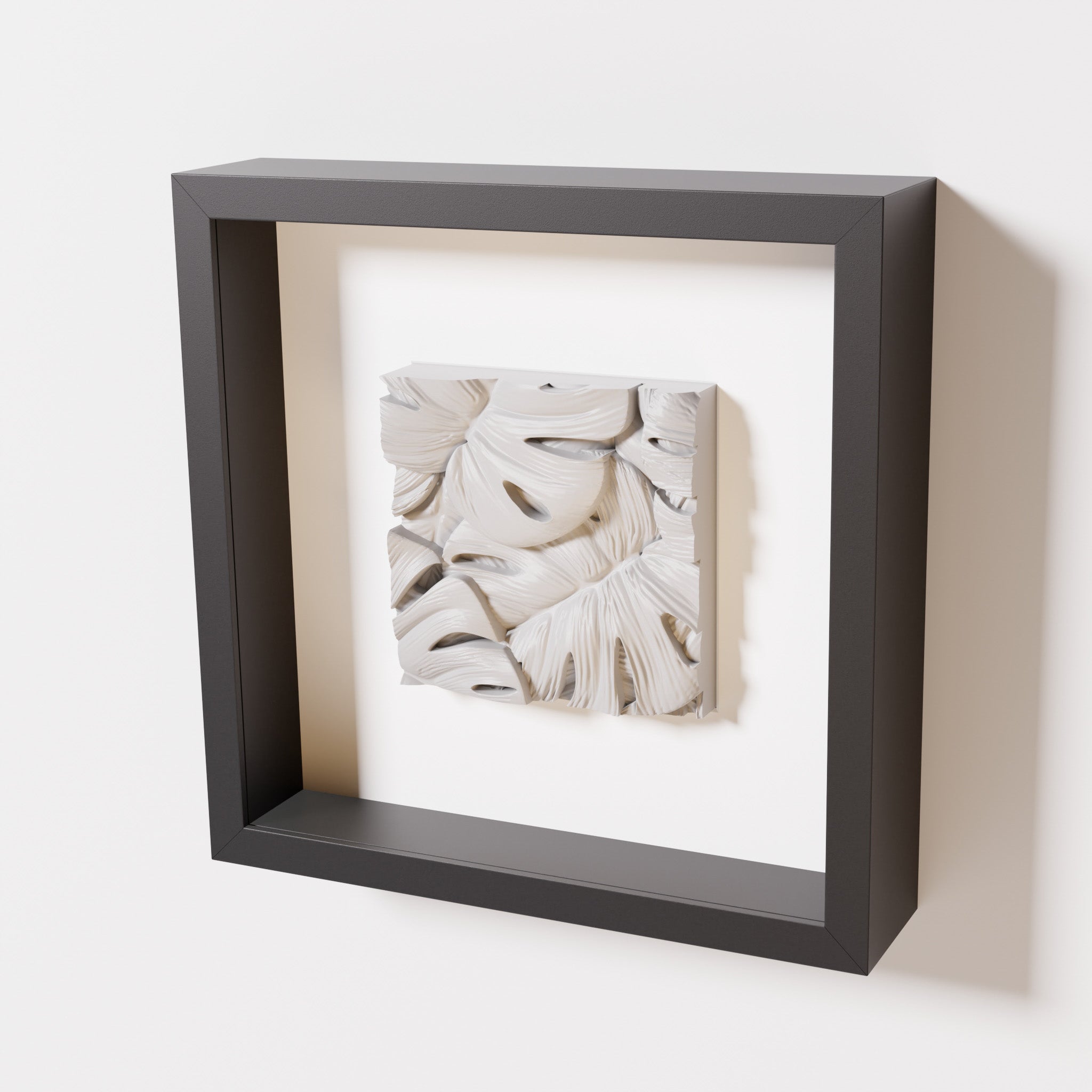 A close-up of a black shadowbox frame containing a marble white artwork featuring layered Monstera leaves, showcasing delicate overlapping details with a soft, smooth texture.