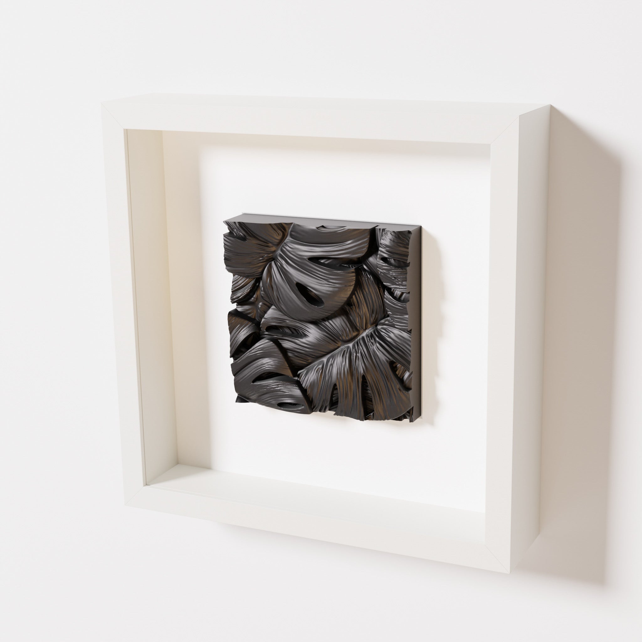 A close-up of a white shadowbox frame containing a matte black artwork featuring layered Monstera leaves, showcasing intricate overlapping details and deep shadows.