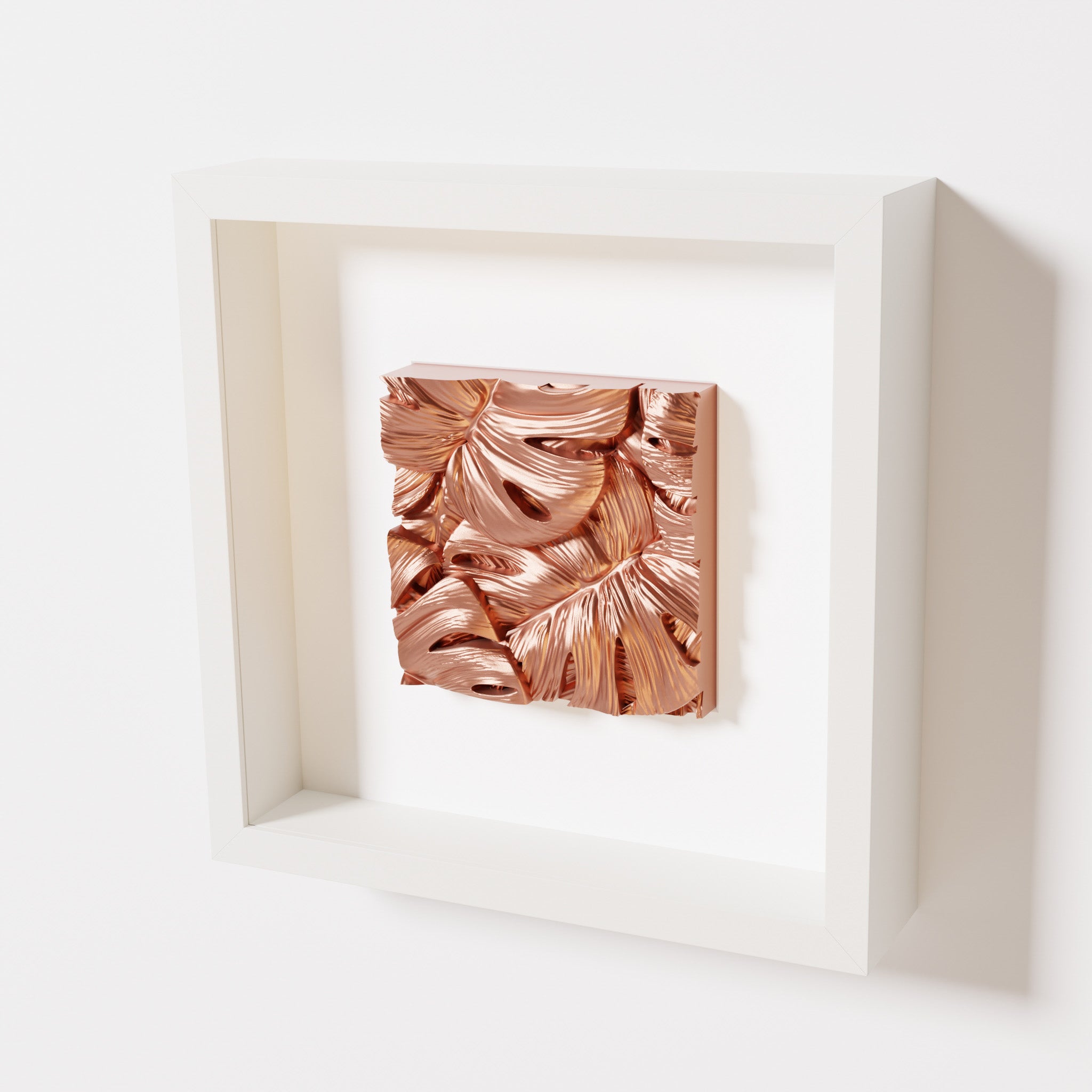 A close-up of a white shadowbox frame containing a chrome copper artwork featuring layered Monstera leaves, showcasing reflective copper highlights and intricate overlapping details.