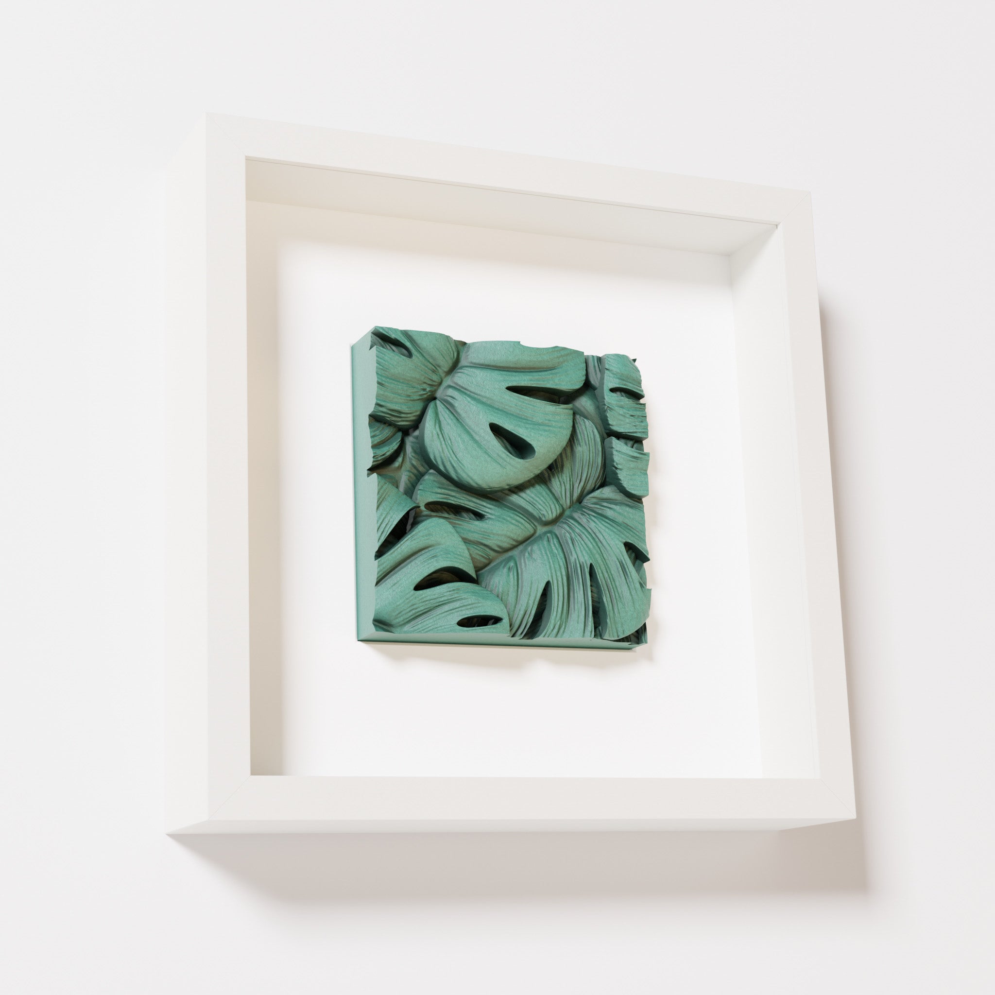 A close-up of a white shadowbox frame containing an old patina artwork featuring layered Monstera leaves, showcasing intricate overlapping details with a textured green finish.