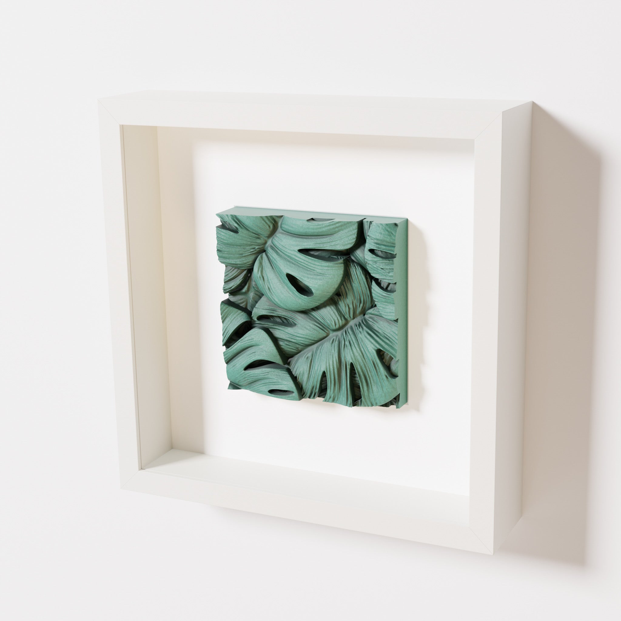 A close-up of a white shadowbox frame containing an old patina artwork featuring layered Monstera leaves, showcasing intricate overlapping details with a textured green finish.