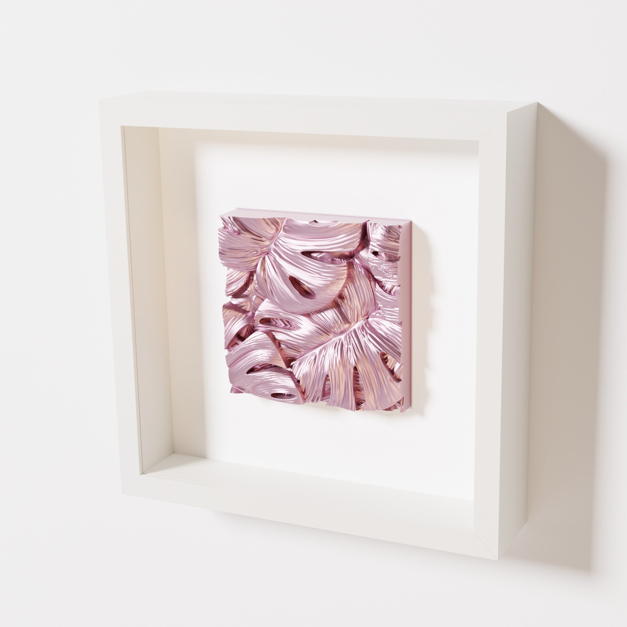 A close-up of a white shadowbox frame containing a metallic rose artwork featuring layered Monstera leaves, showcasing reflective pink highlights and intricate overlapping details.