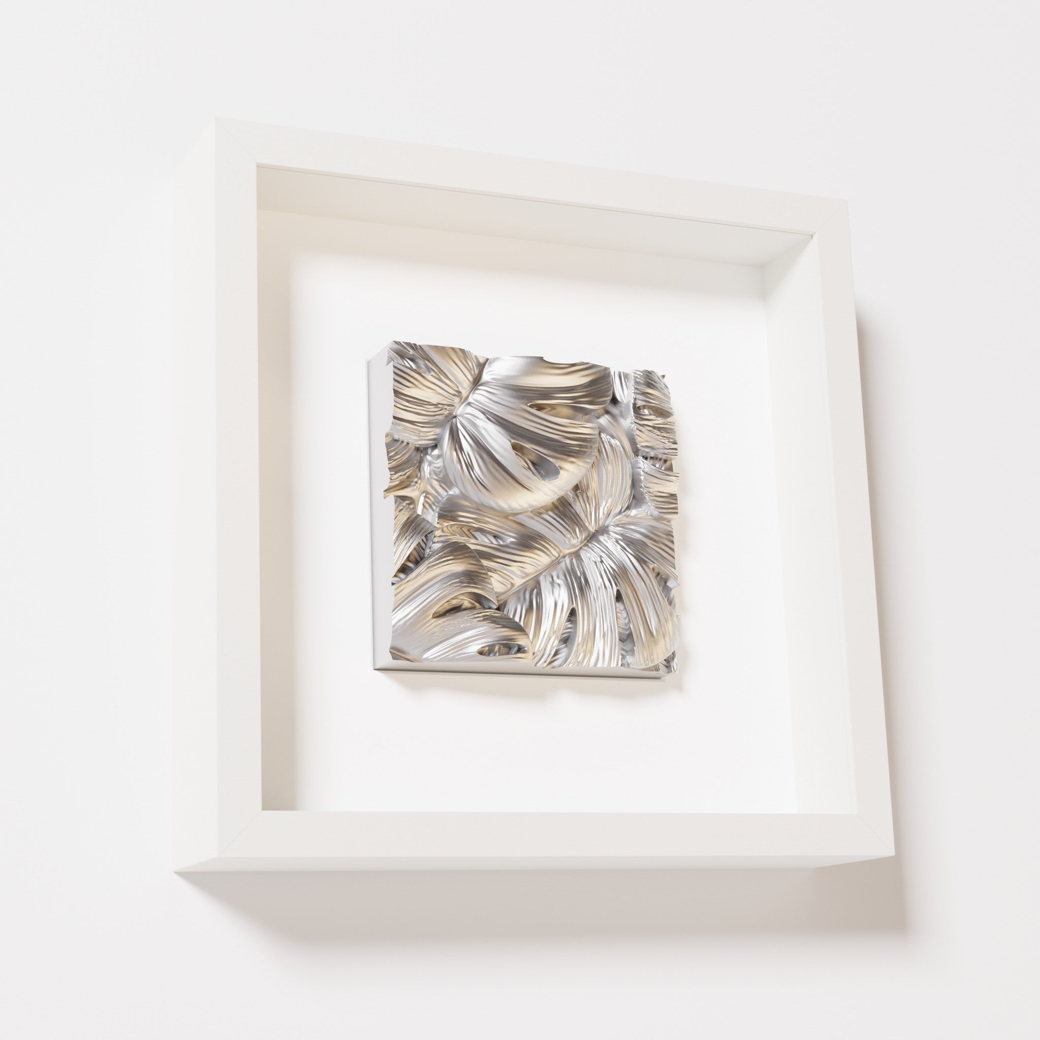 A close-up of a white shadowbox frame containing a chrome silver artwork featuring layered Monstera leaves, showcasing reflective silver highlights and intricate overlapping details.