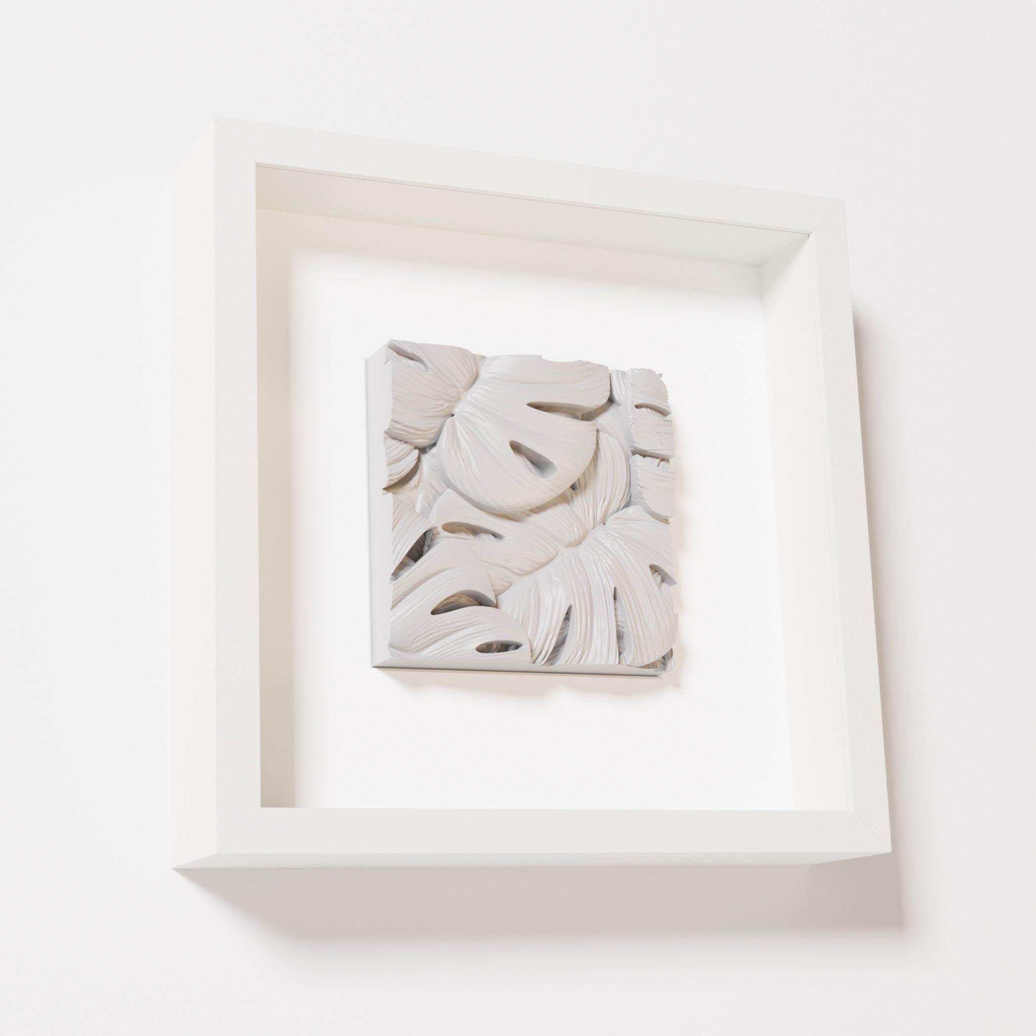 A close-up of a white shadowbox frame containing a marble white artwork featuring layered Monstera leaves, showcasing delicate overlapping details with a soft, smooth texture.