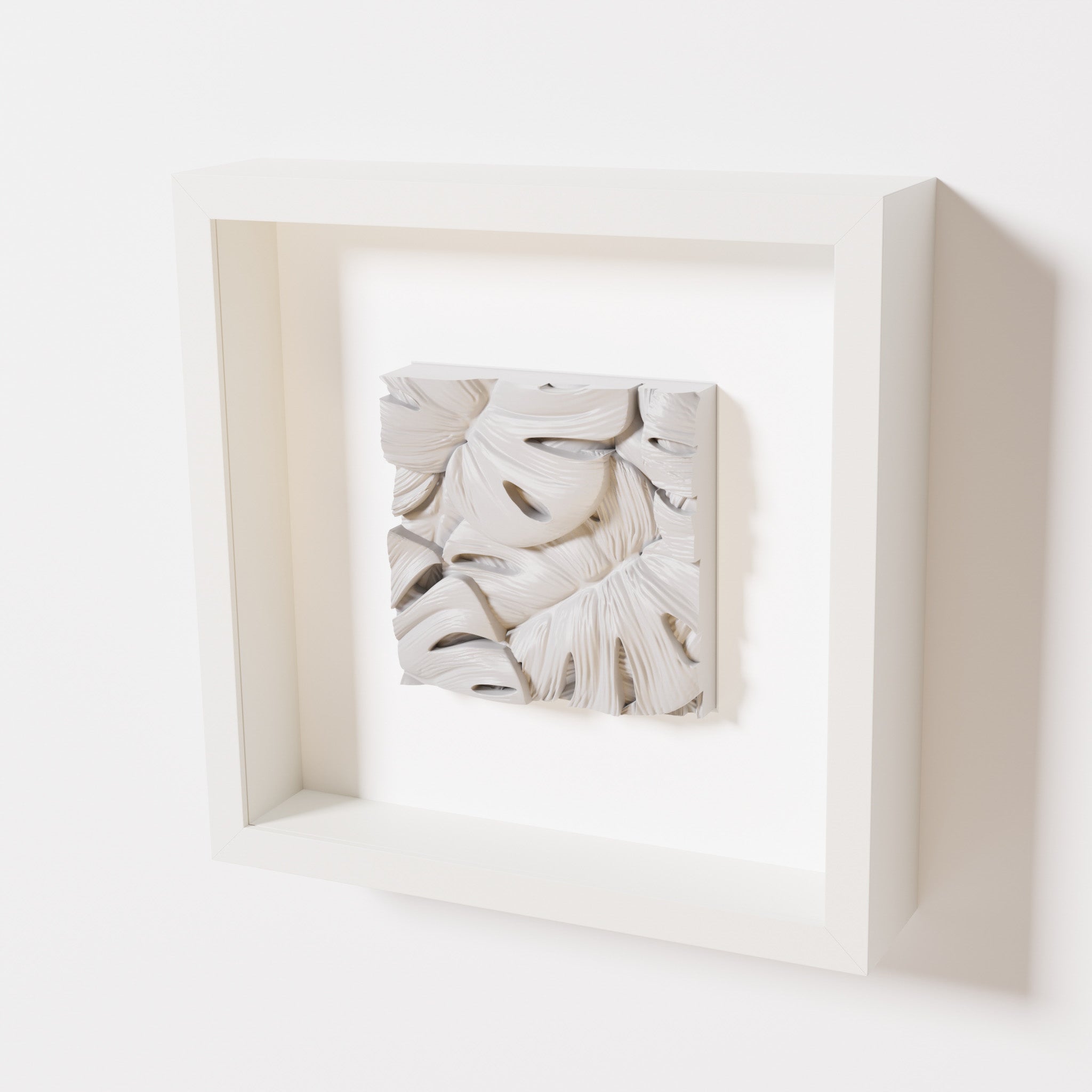 A close-up of a white shadowbox frame containing a marble white artwork featuring layered Monstera leaves, showcasing delicate overlapping details with a soft, smooth texture.