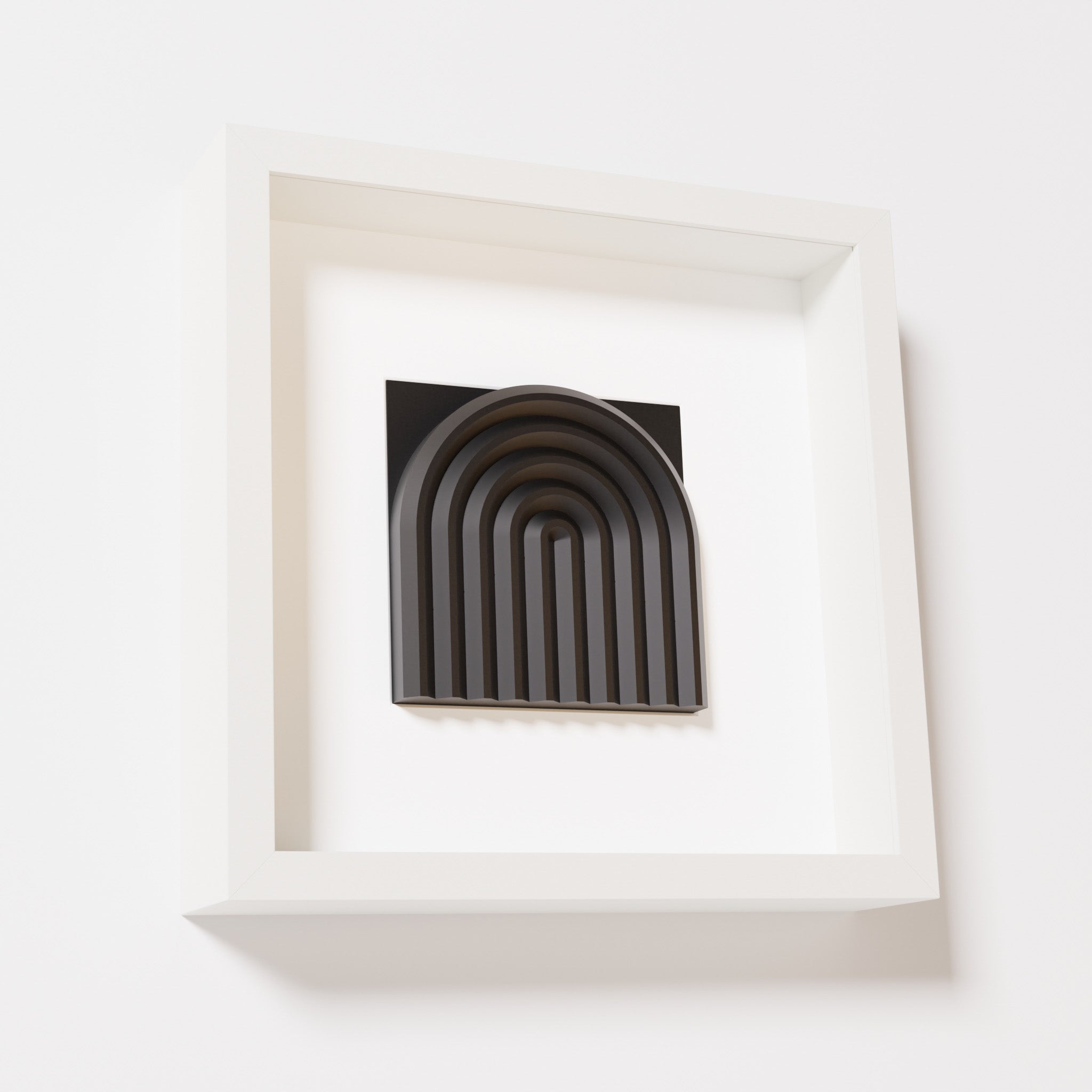 A close-up of a white shadowbox frame containing a matte black artwork featuring the gentle arc of a rainbow design, showcasing its smooth, layered texture and intricate curvature.