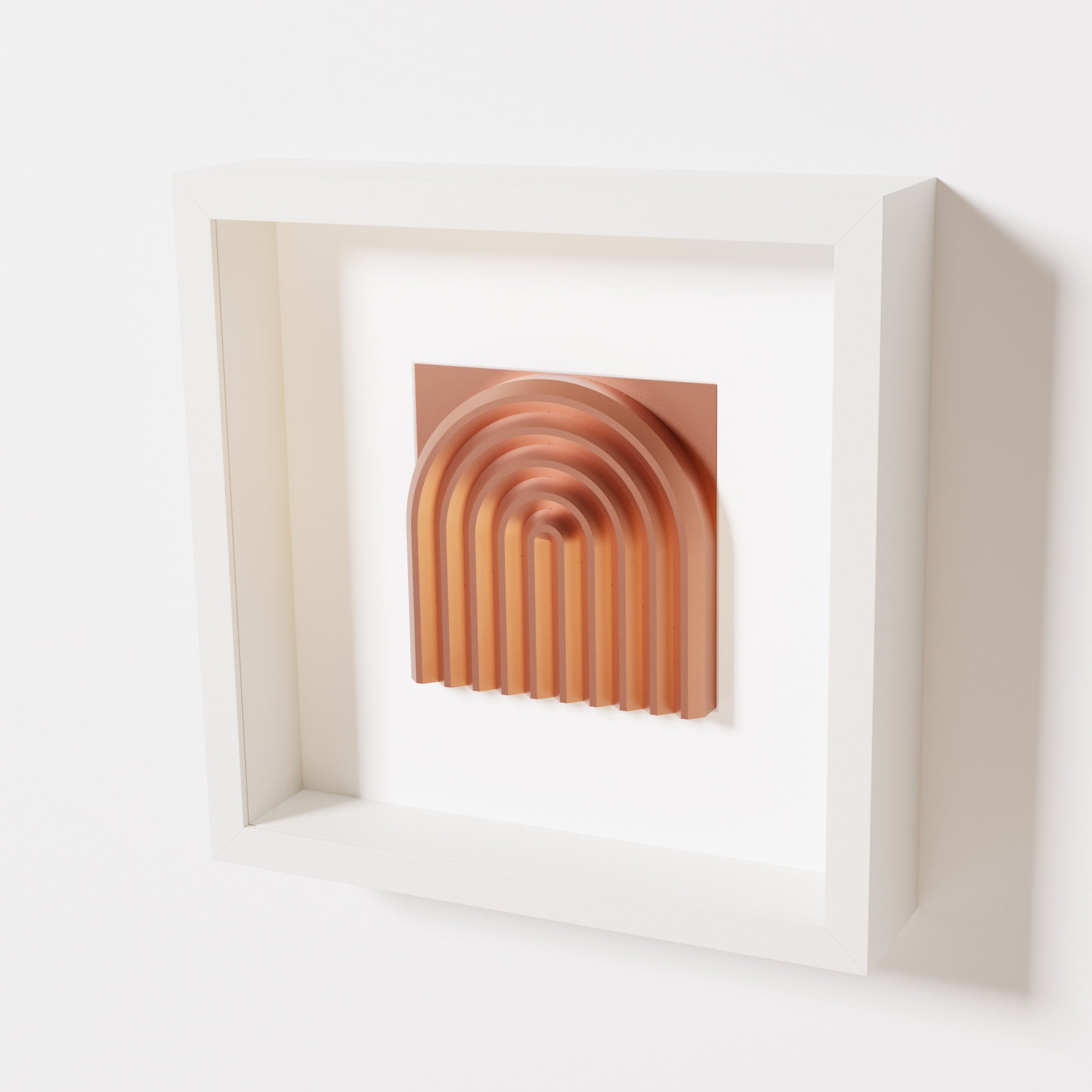 A close-up of a white shadowbox frame containing a chrome copper artwork featuring the gentle arc of a rainbow design, showcasing its shiny copper highlights and layered textures.