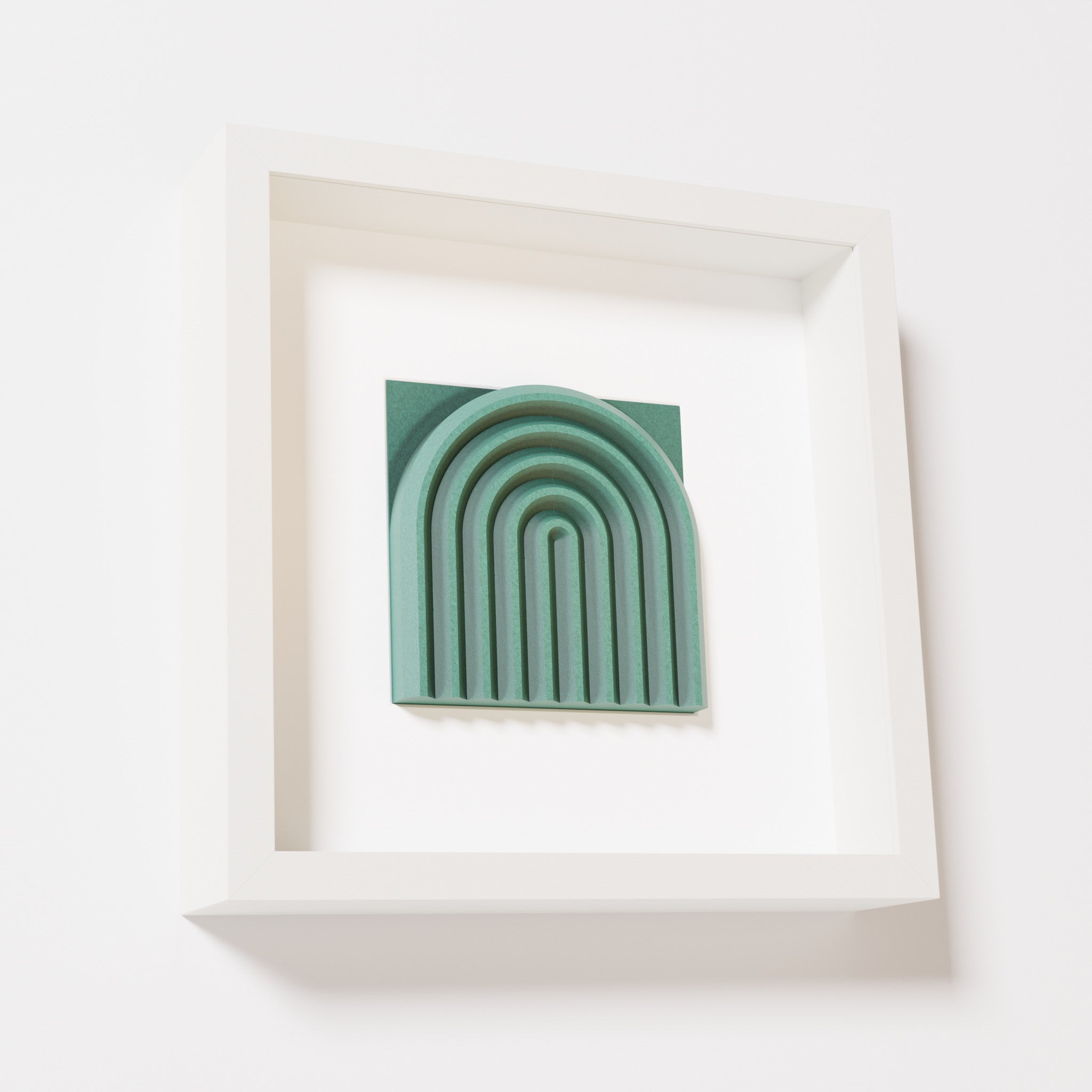 A close-up of a white shadowbox frame containing an old patina artwork featuring the gentle arc of a rainbow design, showcasing its textured green finish and detailed layering.