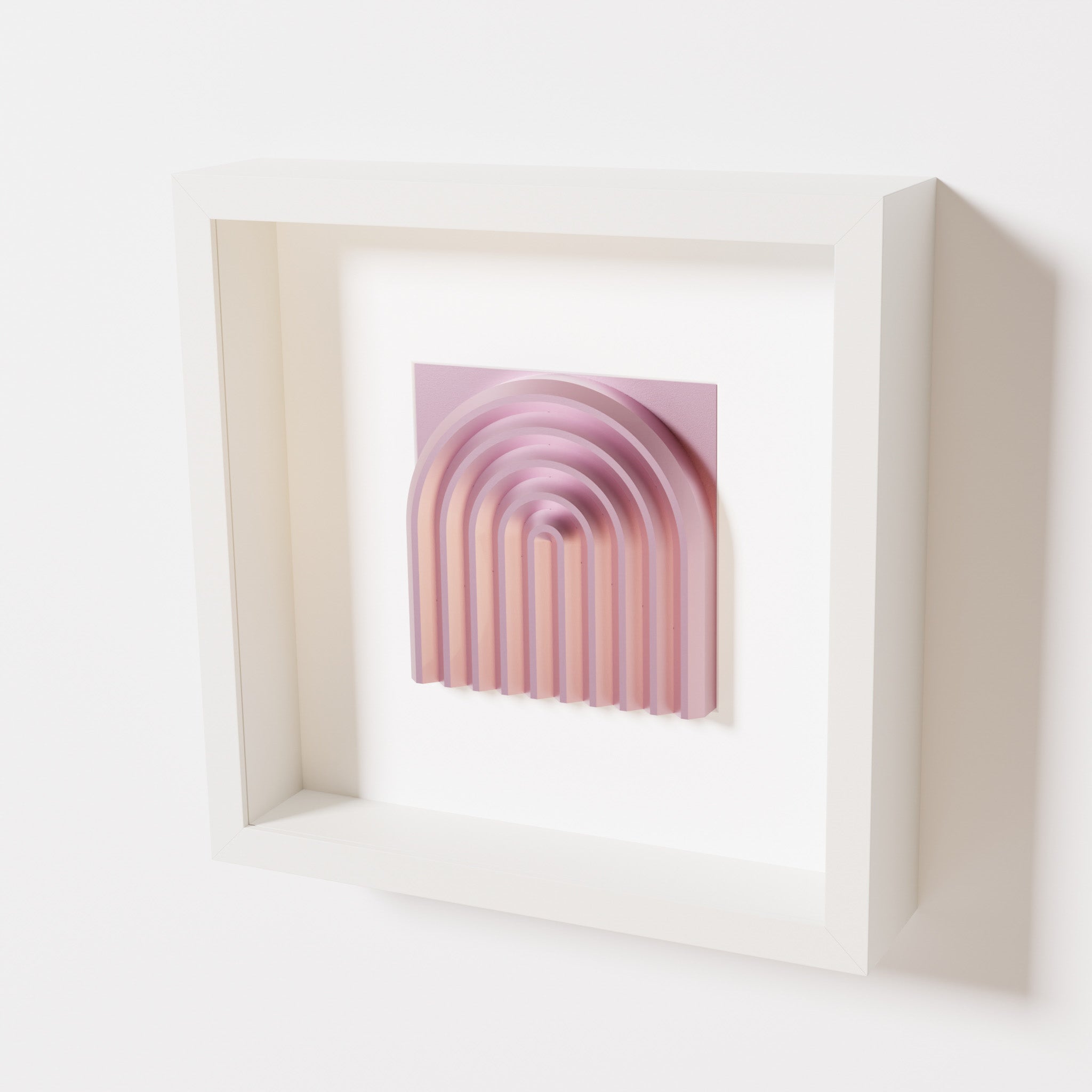 A close-up of a white shadowbox frame containing a metallic rose artwork featuring the gentle arc of a rainbow design, showcasing its soft pink sheen and layered curvature.