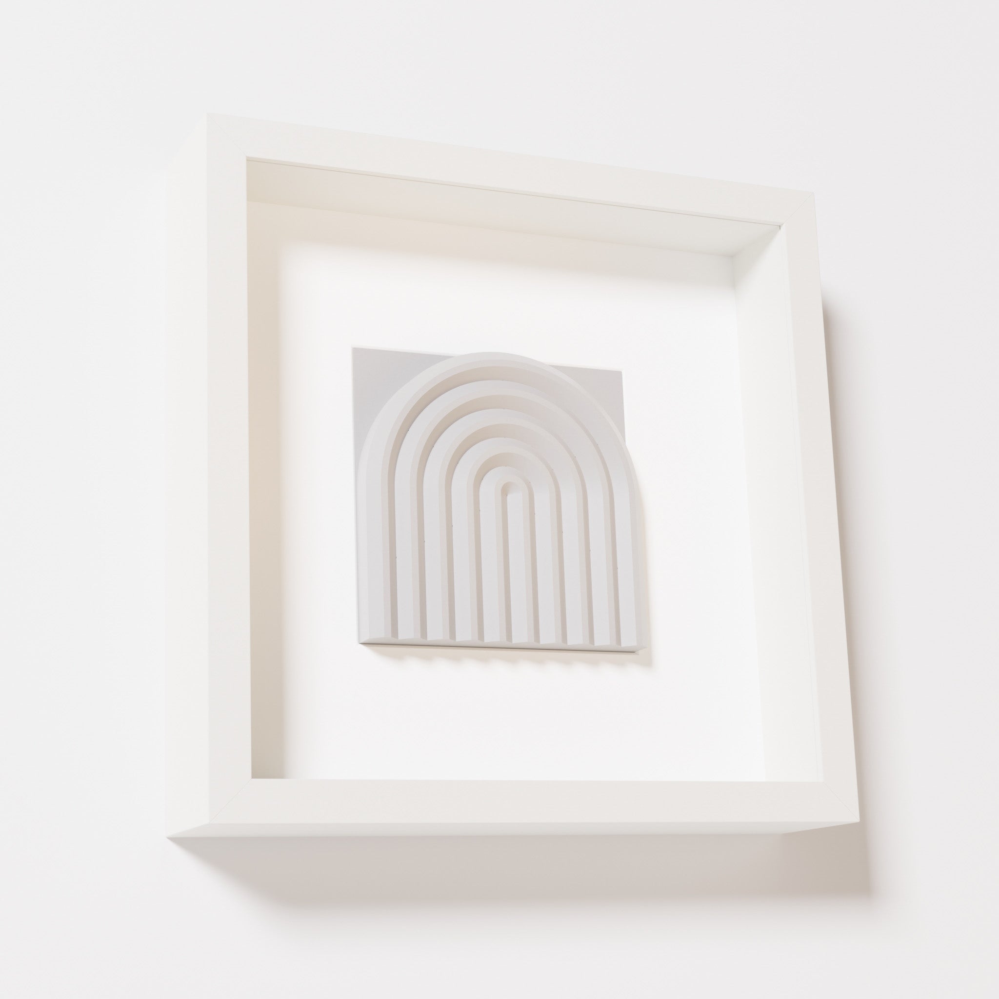 A close-up of a white shadowbox frame containing a marble white artwork featuring the gentle arc of a rainbow design, showcasing its soft texture and detailed curvature.