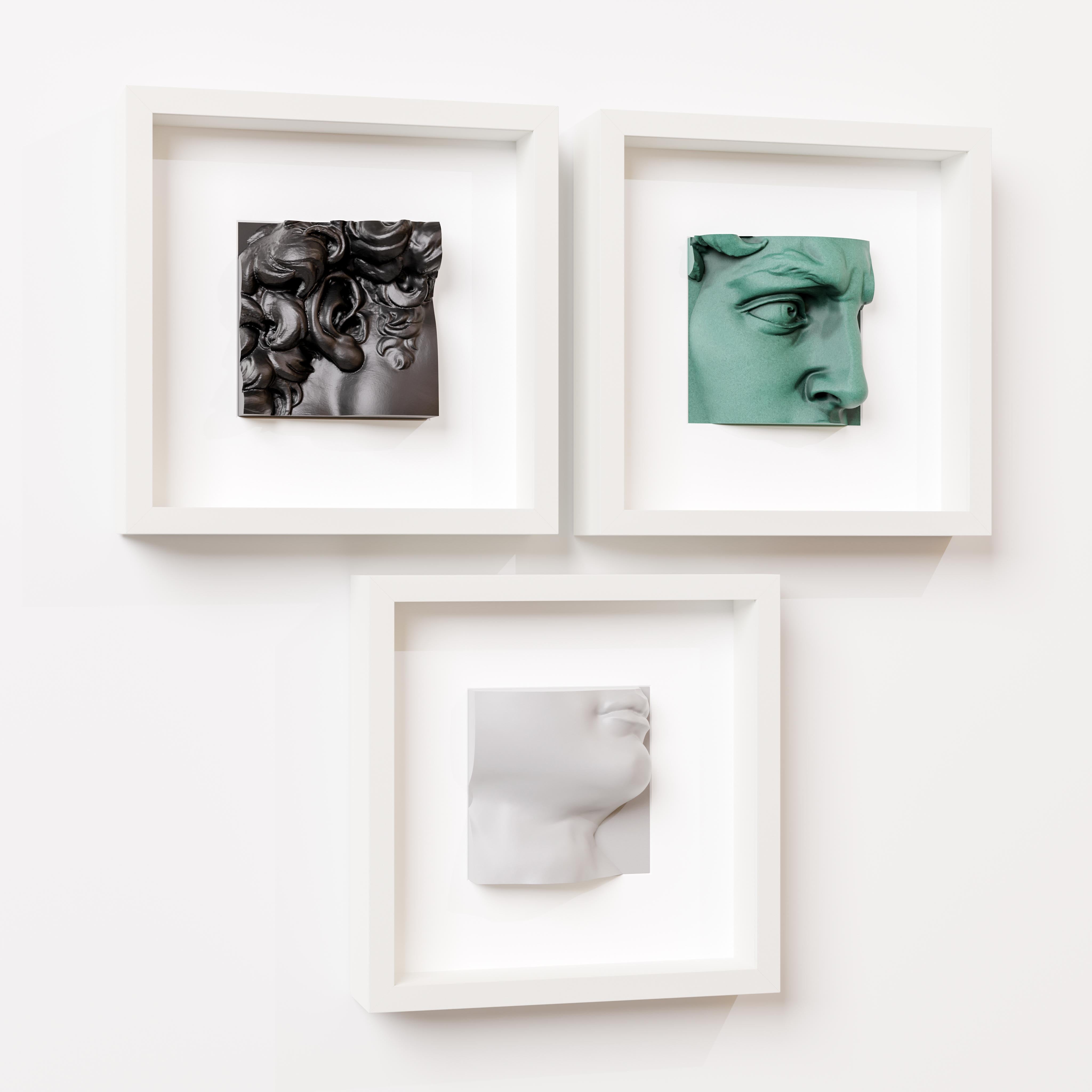 A minimalist arrangement of three white shadowbox frames, each showcasing a unique 3D sculpture: a black intricate Baroque-inspired design, a green classical eye detail, and a white modern profile of a face. Mounted on a clean white wall, this art display highlights a blend of textures, colors, and artistic styles, perfect for contemporary interior decor.